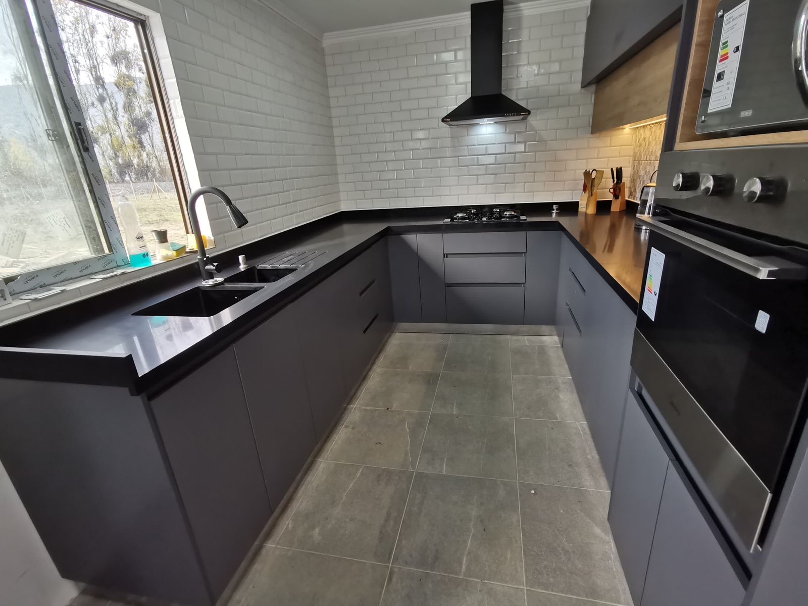 Cocina en U grafito con cubierta negra, revestimiento subway blanco y campana negra