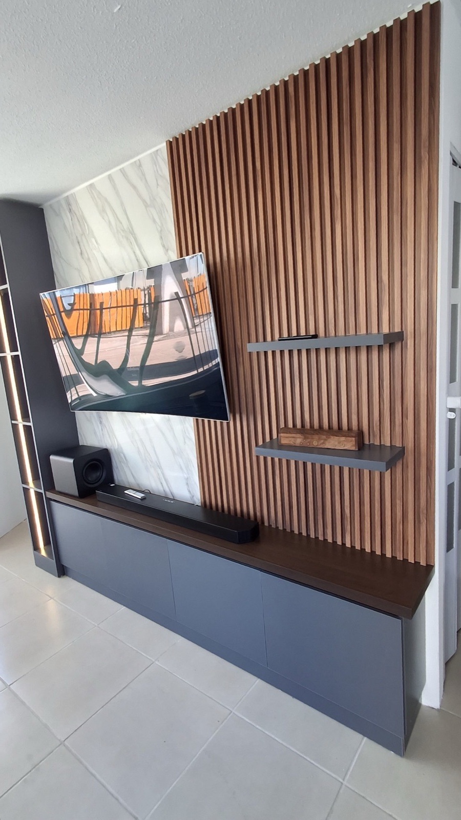 Rack TV + repisero con iluminación Led. Mueble base en melamina gris grafito sin tiradores. Decorativo wall panel en muro con repisas aéreas y lámina de PVC estilo mármol.