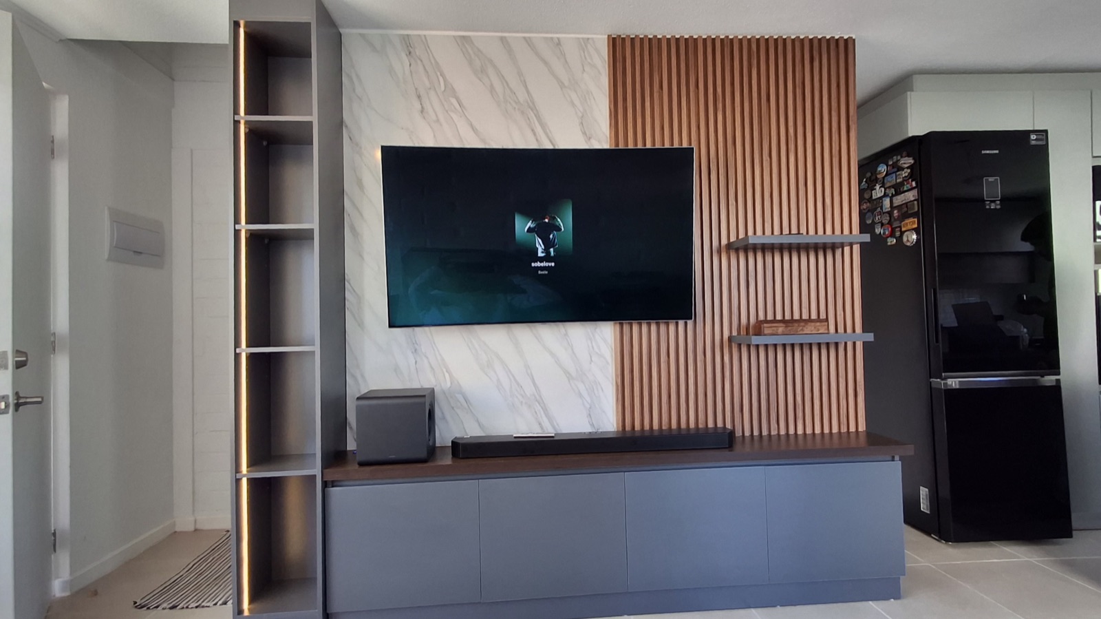Rack TV + repisero con iluminación Led. Mueble base en melamina gris grafito sin tiradores. Decorativo wall panel en muro con repisas aéreas y lámina de PVC estilo mármol.