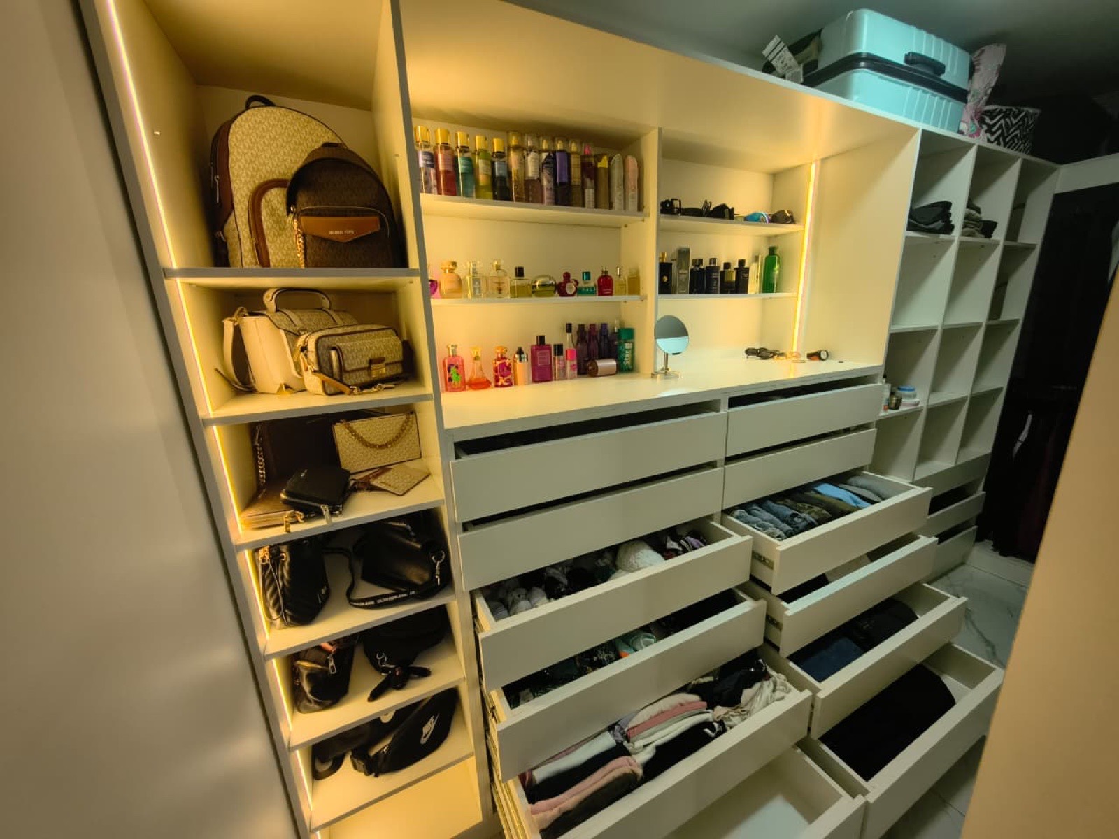 Walk-in closet en U con repisas, iluminación Led, cajoneras y cubículos de almacenamiento.